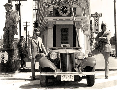 Peter Fox and John Fluevog standing on each side of a car in front of the Hotel Europe in Gastown, Vancouver.