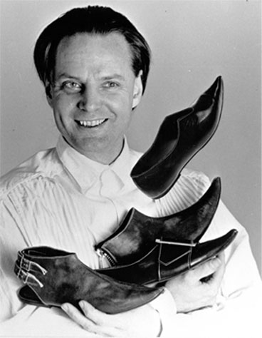 John Fluevog holding four of his shoe designs in his arms.