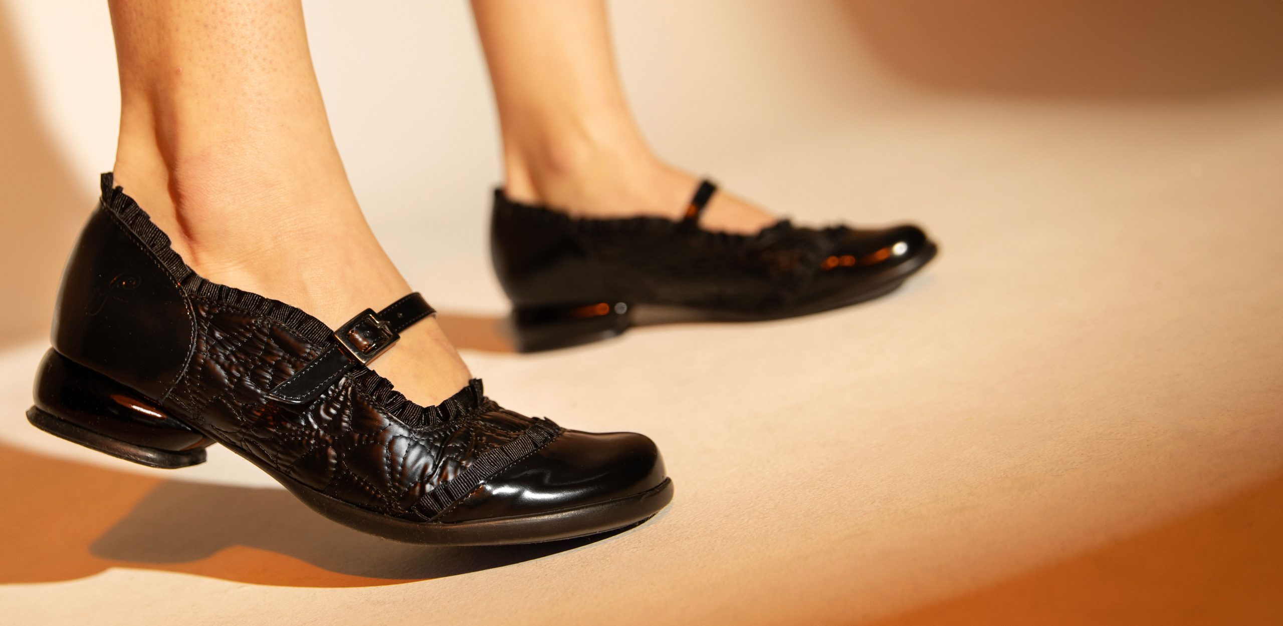 Black John Fluevog Sandz mary-jane shoes, shown from below the ankle. They are quilted and ruffled.